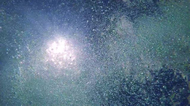 Detail of the water surface with bubbles and sun in the sky - shot from the bottom of the pool - slowmotion