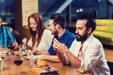 man with smartphone and friends at restaurant