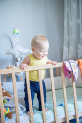 Funny baby standing up in her crib in the room.