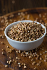 Buckwheat grain on ceramic bowl over wooden table.