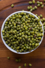Organic mung beans on white ceramic bowl over wooden background.