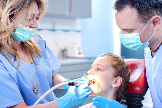 Dentists examining girl patient's teeth at dental office.