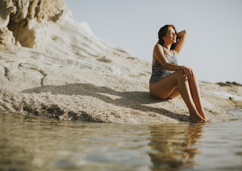 Fototapeta na wymiar Pretty young woman sitting on the rocky shore by sea