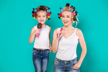 Mother and little daughter in hair curlers on a turquoise background in the studio