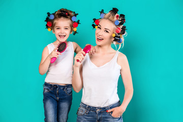 Mother and little daughter in hair curlers on a turquoise background in the studio