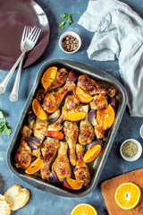 Pieces of chicken baked with oranges and red onions. Top view, vertical photo. On the photo there is a brown plate, forks, a towel, pieces of orange and spices.