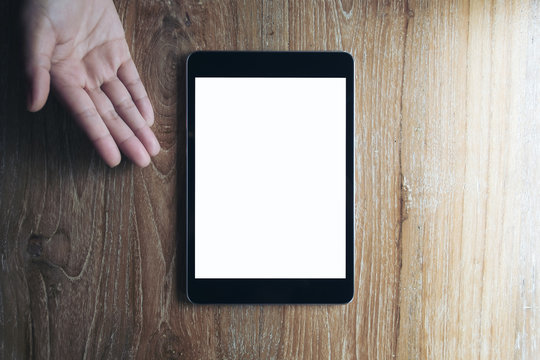 Mockup image of gesturing hand to showing , pointing and presenting a black tablet pc with blank white screen on vintage wooden table background