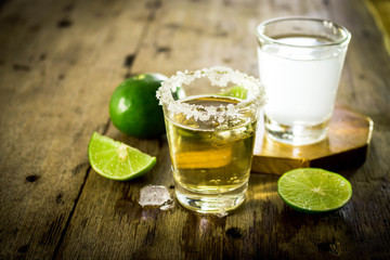 Mexican gold tequila and lime juice shot with lime on wooden table.