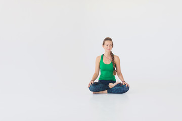 Close up portrait of attractive woman sitting in meditating position on white floor. Young girl raising hands doing yoga.