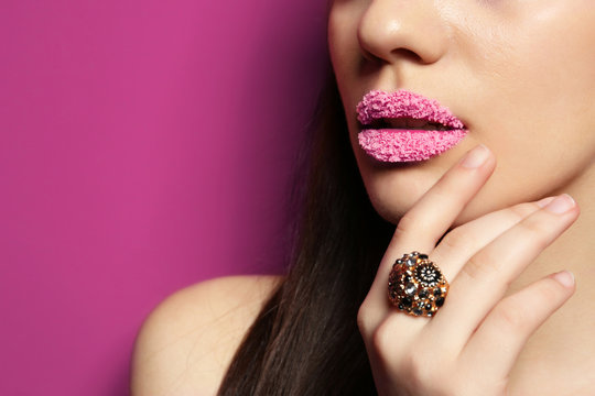 Lips of beautiful young woman covered with sugar on color background