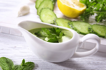 Delicious yogurt sauce in gravy boat with ingredients on kitchen table