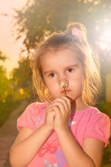 Fototapeta premium Little girl with flower in sunset rays of sun, warm colored background