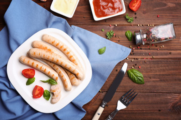 Plate with roasted sausages and tomatoes on wooden background