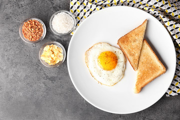 Composition with sunny side up fried egg with toasts and spices on grey table
