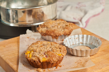 Fresh, baked peach streusel coffee cake and tin mold, cooling on parchment paper on a wood cutting board and napkin