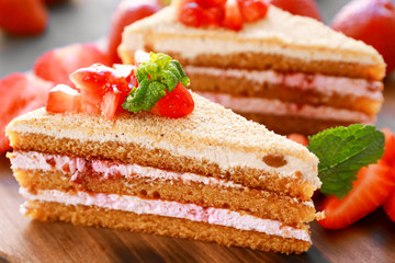 Two pieces of homemade cake with strawberries on wooden board