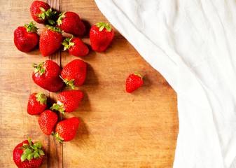Red summer strawberries and white napkin on wooden table, top view