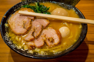 Delicious Japanese Ramen noodles with chopsticks over the soup in a wooden background