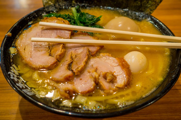 Delicious Japanese Ramen noodles with chopsticks over the soup in a wooden background