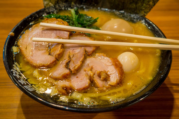 Delicious Japanese Ramen noodles with chopsticks over the soup in a wooden background