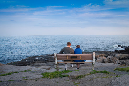 Two lovers peacefully sitting on a bench by the ocean