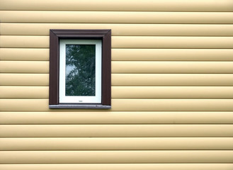 Building wall finished with beige siding panels with small vertical plastic window protect house from bad weather conditions horizontal photo front view