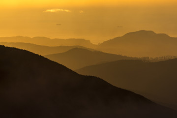 golden hour over some coastal mountains with ships in the bay beyond 