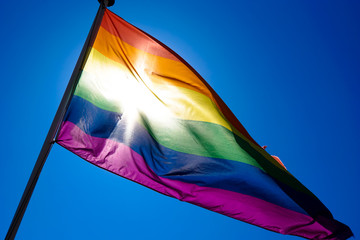 Rainbow flag waiving in the wind with sun shining through it