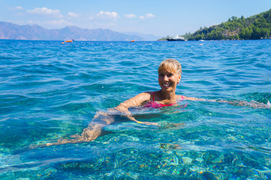 A lady enjoys in the sea. Lady splashing sea water and enjoying life during summer holidays on the tropical beach. Woman swim and relax in the sea. 
