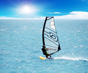 A windsurfing in the sea surfs fast to the sun