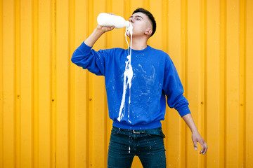Stylish serious guy in a blue sweater, drinks and spills milk or yogurt
