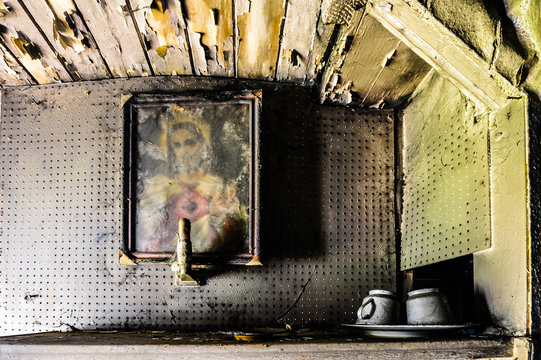 A sacred heart picture of Jesus hangs on the wall of a very dirty house with peeling paint