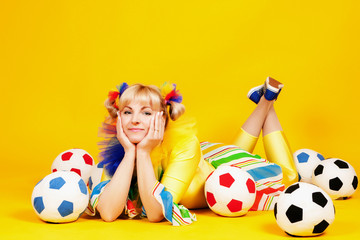 Merry clown girl lying on the floor. Clown on a yellow background. Sports activities for children....