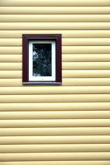 Building wall finished with beige siding panels with small vertical plastic window protect house from bad weather conditions horizontal photo front view