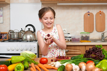 child girl posing with handful of cherries, fruits and vegetables in home kitchen interior, healthy food concept