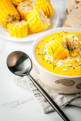 Vegan cuisine. Traditional autumn corn soup. Served with corn cobs, greens, cream. On a white marble table. Copy space