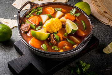 Autumnal vegetable stew. Mexican traditional vegetable soup Mole de olla with meat, potatoes, carrots, beans, corn and lime. Copy space