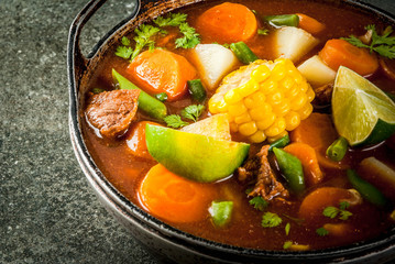 Autumnal vegetable stew. Mexican traditional vegetable soup Mole de olla with meat, potatoes, carrots, beans, corn and lime. Copy space