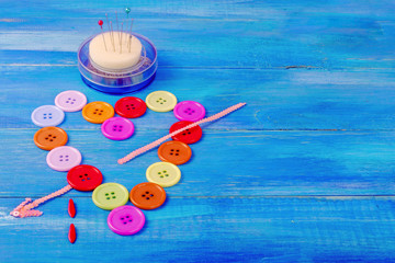 Multicolored buttons in the form of a heart, pierced by an arrow from a tape on a blue wooden background.