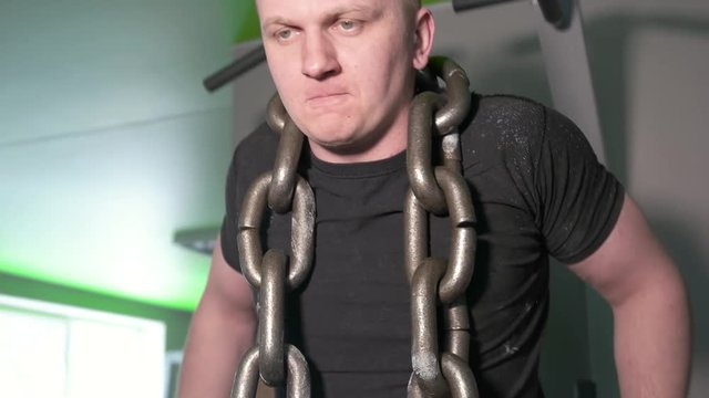 Athlete in gym doing exercises on parallel bars with chain around his neck