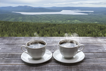 Two cups of fresh hot coffee for a pair of lovers against the backdrop of mountains, lakes, forest. Nature.