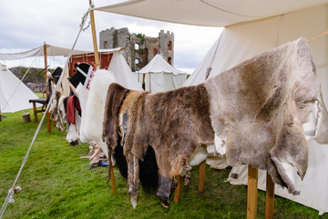 Animal hides hang out to dry at a medieval camp beside a ruined castle.
