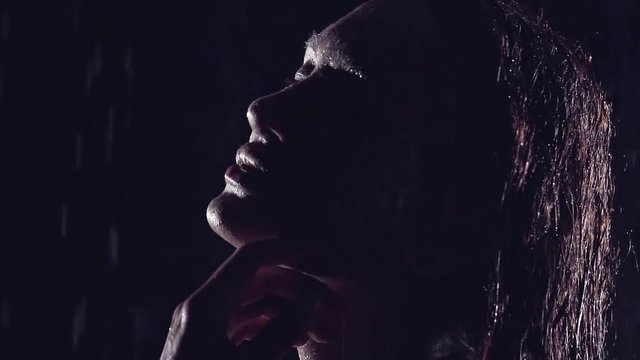 close-up. silhouette of sexy girl with large plump lips. she stands in the rain and dreamy touching her fingers behind his neck and chin.