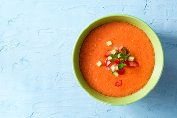 Summer cold soup gazpacho with parsley and vegetables on blue concrete background.