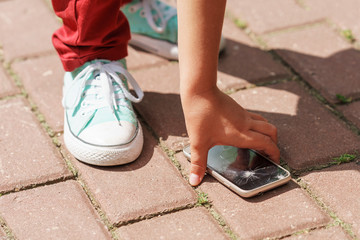 child picks up the phone with a broken screen from the sidewalk
