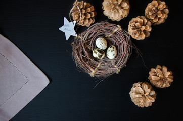 Nest with quail eggs and cones on a black background with a signature Hello autumn