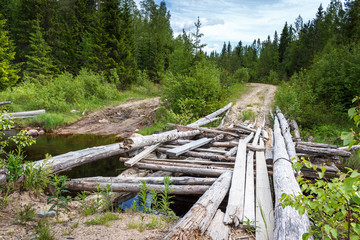 Fototapeta na wymiar Old ruined wooden bridge on a dirt road in the forest