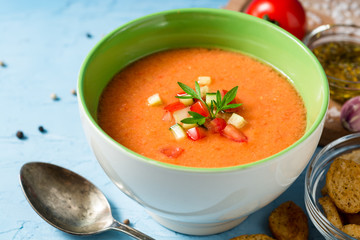 Summer cold soup gazpacho with parsley and vegetables on blue concrete background.