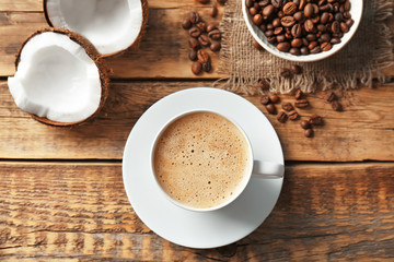 Cup of tasty coconut coffee and beans on wooden table