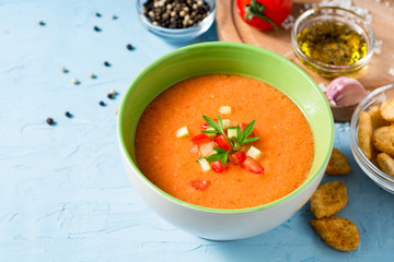 Summer cold soup gazpacho with parsley and vegetables on blue concrete background.